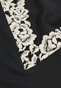 Schwarzer Stoff mit komplizierter cremefarbener Blumen-Spitze entlang einer diagonalen Kante, die Detail- und Texturkontraste hervorhebt.