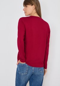 Rode lange mouwen shirt van zachte stof, met een ronde halslijn en een relaxte pasvorm, gecombineerd met lichtblauwe jeans.
