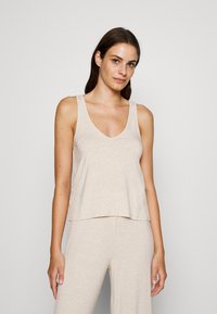 Beige cotton tank top with a V-neck, wide straps, and a relaxed fit. Soft texture, simple design, and no visible patterns or hardware.