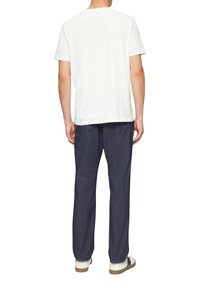 Weißes Baumwoll-T-Shirt, kombiniert mit dunkelblauen Hosen, die einen lockeren Schnitt und eine subtile Textur aufweisen, ergänzt durch weiße Sneakers.