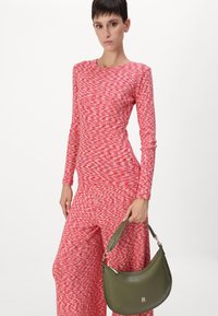 Red and white patterned long-sleeve jumpsuit with wide legs, paired with a green leather shoulder bag featuring a curved shape and logo accent.