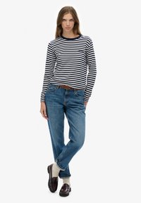 Langærmet stribet top i navy og hvid, blå jeans, brune loafers, beige sokker og et brunt bælte. Simpelt, afslappet outfit på en model.