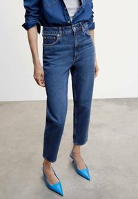 Jean en denim bleu taille haute avec une coupe droite, présentant une double couture et des boutons en métal, assorti à des escarpins pointus bleus brillants.