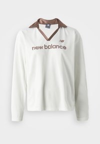 Weißes Netz-langarmshirt mit einem braunen Satin-Kragen. Verfügt über das braune "new balance"-Logo auf der Vorderseite. Lässiges Sportdesign.