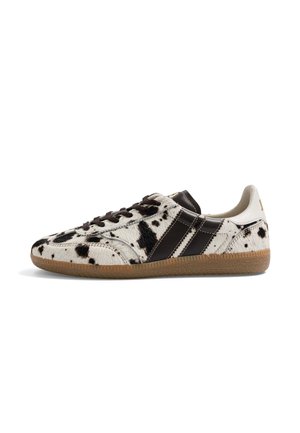 Basket basse avec imprimé vache noir et blanc, rayures marron foncé, lacets noirs et semelle en gomme, vue de côté sur fond blanc.