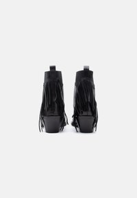 Ghete negre până la gleznă cu detalii cu franjuri, realizate din piele lucioasă, cu toc înalt și gros și două curelușe pentru ușurința încălțării.
