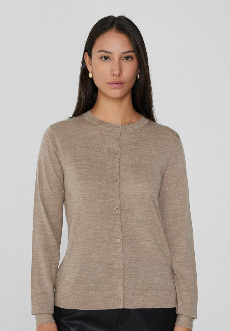Beige gestrickte Freizeitjacke mit Rundhalsausschnitt und langen Ärmeln, die eine Knopfleiste und ein dezentes strukturiertes Muster aufweist.