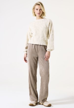 Pull crémeux et duveteux à manches longues, associé à un pantalon en velours côtelé beige clair. Des baskets beiges à enfiler sont mises en avant. Design simple.