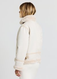 Giacca color crema con colletto e polsini in faux fur, dotata di dettagli in pelliccia e una vestibilità rilassata. Il materiale sembra morbido e caldo.