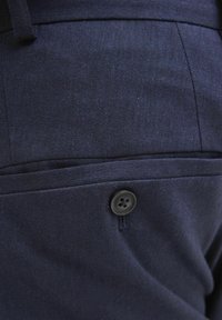 Pantalons bleu marine avec un tissu texturé, une poche latérale et un détail de bouton noir, mettant en valeur un design épuré et ajusté.