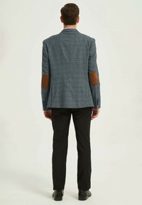Blazer à carreaux gris avec des coudières marron, fente simple et revers standard, associé à un pantalon noir et des chaussures noires.