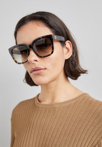 Lunettes de soleil carrées surdimensionnées avec des montures en écaille de tortue et des verres dégradés bruns, présentant des accents de logo dorés sur les branches.