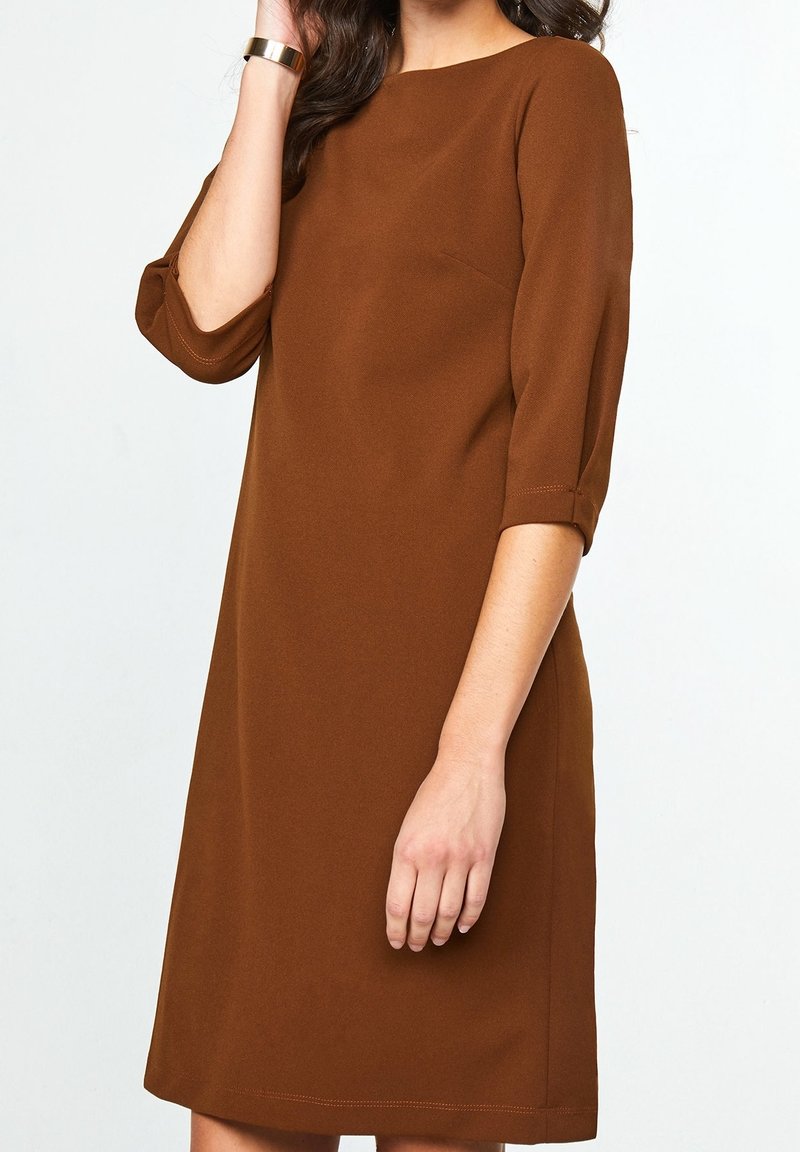 Brun skiftklänning med rund halsringning, trekvartslånga ärmar och slät tyg. Har en diskret sidfickseam.