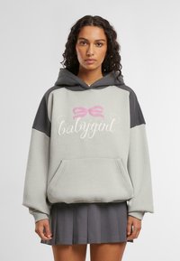 Lys grå hettegenser med mørkegrå bærestykke, med et rosa sløyfe-graphic og hvit tekst "babygirl." Inkluderer en frontlomme.