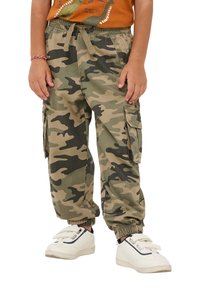 Pantaloni cargo mimetici in tonalità di verde e beige, con polsini elastici, vita con cordoncino e tasche laterali. Indossati con sneakers bianche.