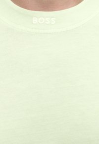 Gros plan sur le col d'un t-shirt jaune pâle avec le texte brodé en relief "BOSS" centré sous le col.