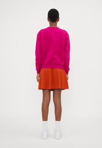 Ljusröd sweatshirt med långa ärmar kombinerad med en utsvängd orange kjol. Vita ankelsockar och vita sneakers i casual stil kompletterar looken.