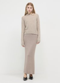 Pull beige en maille à manches longues, associé à une jupe maxi taupe clair ajustée. Le mannequin porte des chaussures noires à talons bas.