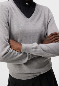 Ljust grå V-ringad tröja i mjukt tyg, med ribbade muddar och nederkant. Kombination med en svart polotröja under.