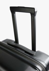 Maleta rígida negra con un mango telescópico y superficie texturizada, además de un mango superior separado para facilitar el transporte.