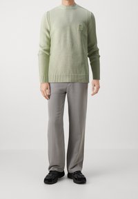 Ljusgrön stickad tröja med ribbat nederkant och ärmslut, med en liten logotypapplikation. Kombinerad med grå raka byxor och svarta sneakers.