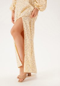 Geel bloemen maxi-jurk met zijschede, lange pofmouwen en beige blokhakken. Licht materiaal met een zachte textuur.