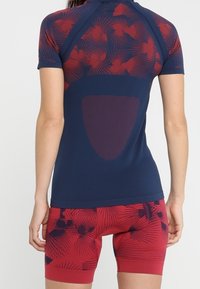 Kortärmad atletisk topp i marinblått med röd blommönster, tillsammans med röda shorts med ett matchande blommönster. Strukturerad tyg med stödjande passform.