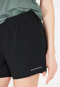 Svarta träningsshorts med resårmidja och logotyp i vit text på nedre vänstra sidan. Slät tygkvalitet med en lättviktsdesign.