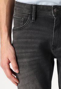 Jean en denim gris foncé avec une texture lisse, coupe slim et design classique à cinq poches, doté d'une fermeture à un bouton et de passants de ceinture.