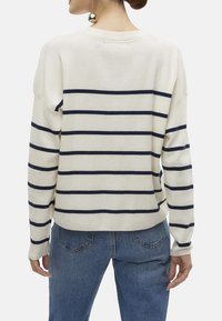 Maglione leggero crema con strisce orizzontali navy, vestibilità ampia, scollo rotondo e polsini a coste. Abbinato a jeans in denim blu.