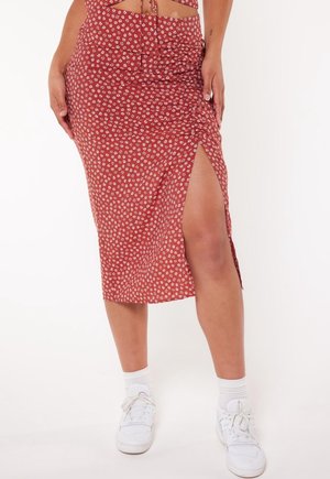 Kvinde iført en rustfarvet midi nederdel med hvidt blomsterprint og lårhøjt slids, kombineret med hvide sneakers og sokker.