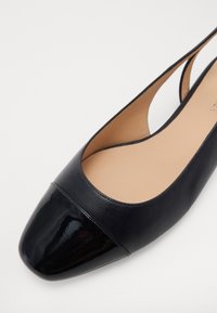 Ballerines noires à bout rond, avec un embout en cuir verni brillant, un dessus en cuir lisse et un design avec des découpes sur les côtés.