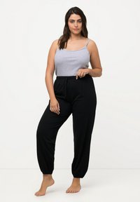 Graues Tanktop mit dünnen Trägern; schwarze, locker sitzende Hose, die am Knöchel gerafft ist; weicher Stoff; minimalistisches Design; barfuß.