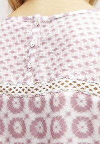 Blusa leggera e a fantasia con un design geometrico rosa e bianco, chiusura con bottoni e dettagli in pizzo sul retro.