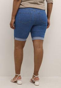 Pantalones cortos bermuda de mezclilla en azul medio, con dobladillo enrollado, diseño ajustado, bolsillos traseros y una textura suave.