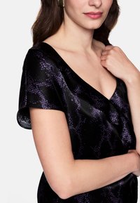 Black dress featuring a purple snake print, v-neckline, and short sleeves, made of a smooth, shiny fabric. Subtle folds add texture.