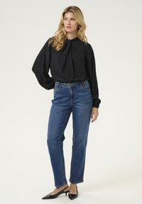 Juoda ilgomis rankovėmis palaidinė su plisuotu kaklu, derinama su mėlynomis tiesiomis džinsomis ir juodais slingback aukštakulniais. Paprastas, elegantiškas derinys.