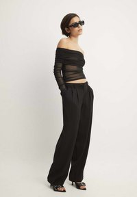 Čierny off-the-shoulder sieťový top s vrstvenými detailami, skombinovaný s čiernymi nohavicami s vysokým pásom a čiernymi sandálmi na podpätku. Čierne obdĺžnikové slnečné okuliare.