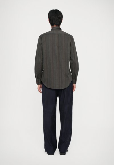 Camisa de botón de rayas oscuras con mangas largas, que presenta un cuello y un ajuste relajado, combinada con pantalones azul marino a rayas.
