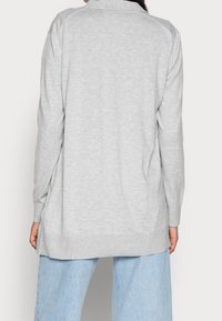Hellgrauer langärmeliger Pullover mit geripptem Saum und Bündchen. Weiche Textur, klassischer Schnitt und Rückenkrauldetail. Kombiniert mit hellen Jeans.