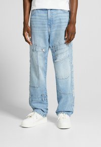 Vaaleansiniset farkkukangasta cargo-housut rentoa leikkausta, useilla taskuilla ja kontrastivärisellä ompeleella. Yhdistettynä valkoisiin lenkkareihin.