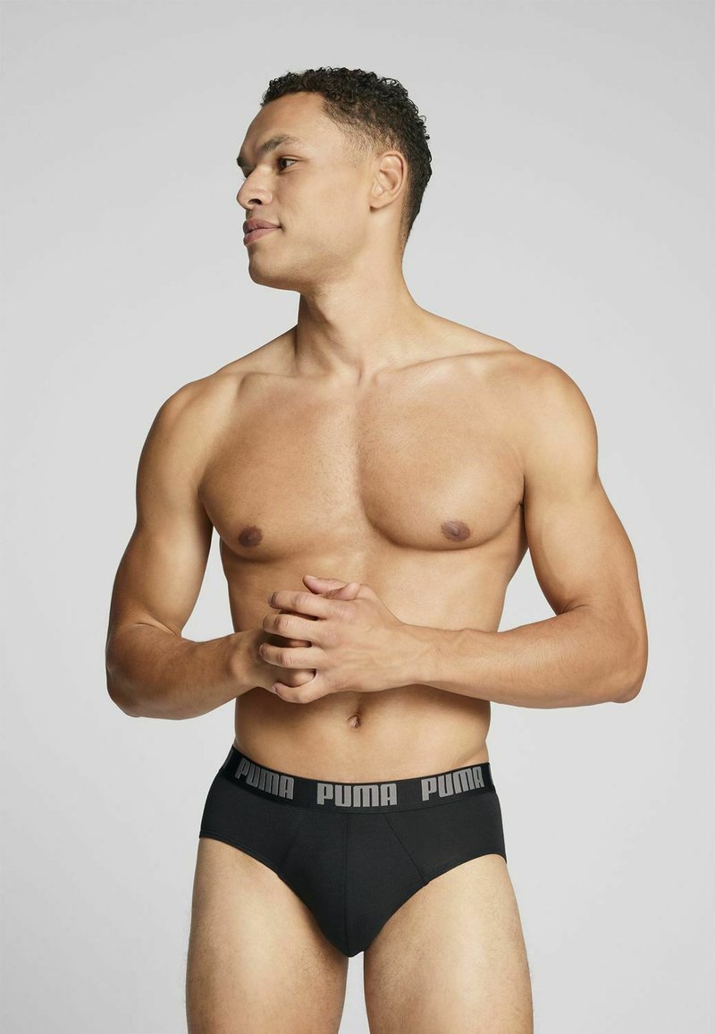 Schwarze kurze Unterwäsche mit einem strukturierten Bündchen, das das "PUMA"-Logo in Grau trägt, von einem männlichen Modell in Seitenansicht getragen.