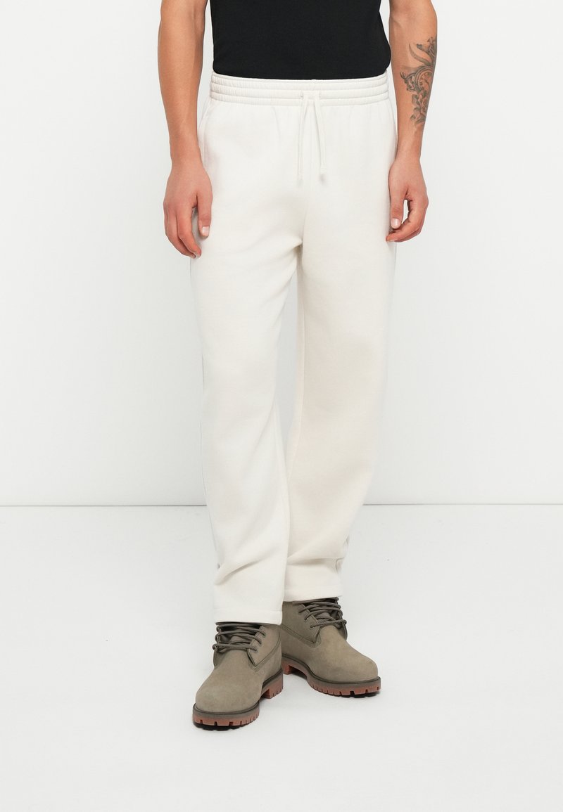Pantalones de chándal blancos con una cintura elástica y cordón. Combinados con botas grises hasta el tobillo con una suela gruesa y cordones.
