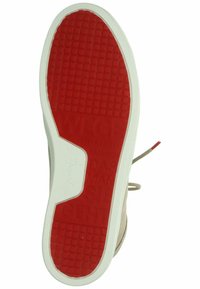 Beige skosula med en strukturerad vit kant och en röd gummiunderdel som har ett rutmönster. Präntad text synlig på den röda sektionen.