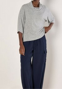 Graues Oberteil mit Wasserfallausschnitt und lockerer Passform. Kombiniert mit marineblauen, weiß gestreiften, weitem Hosen mit Seitentaschen und Kordelzug in der Taille.