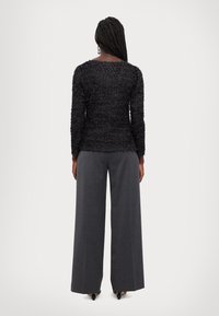 Schwarzes, texturiertes Langarmshirt mit Rundhalsausschnitt, kombiniert mit grauen, weit geschnittenen Hosen, die eine glatte Oberfläche und subtile Tailoring-Details aufweisen.