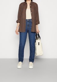 Camicia a righe marrone e nera, top beige, jeans blu, sneakers bianche e una borsa crema con manici neri.