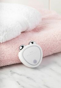 White facial massager with two silver knobs, labeled "STYLPRO," rests on a pink towel next to a white textured towel on a marble surface.