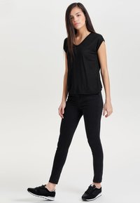 Sort v-hals t-shirt med korte ærmer, parret med slim-fit sorte jeans og sorte sportssko med hvide detaljer. Glat tekstur.