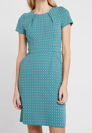 Woman wearing a fitted short-sleeve blue dress with a small diamond pattern and pleats near the round neckline.